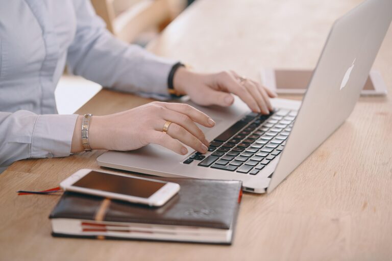 Vrouw werkt op laptop met agenda, telefoon en tablet naast zich, voor overzicht en planning